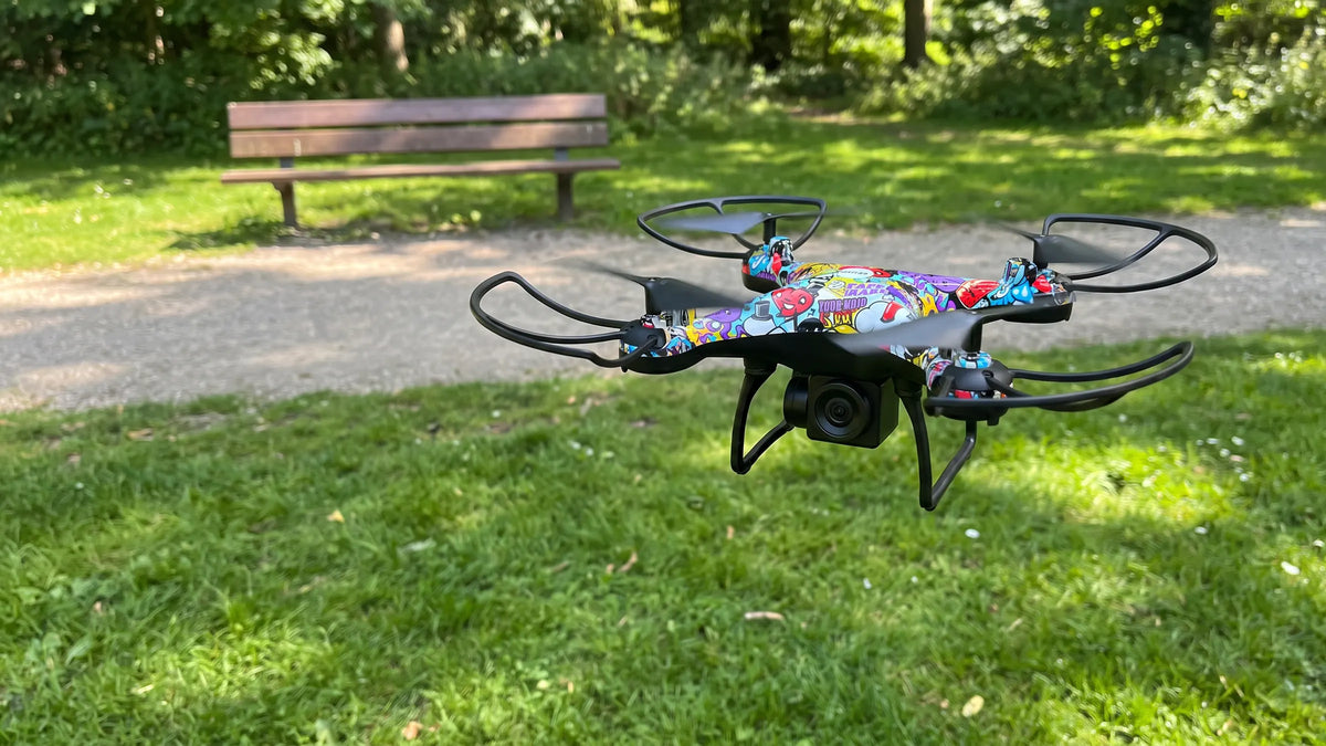 Denver DCW340 drone zweeft laag boven het gras in een park, camera naar de kijker