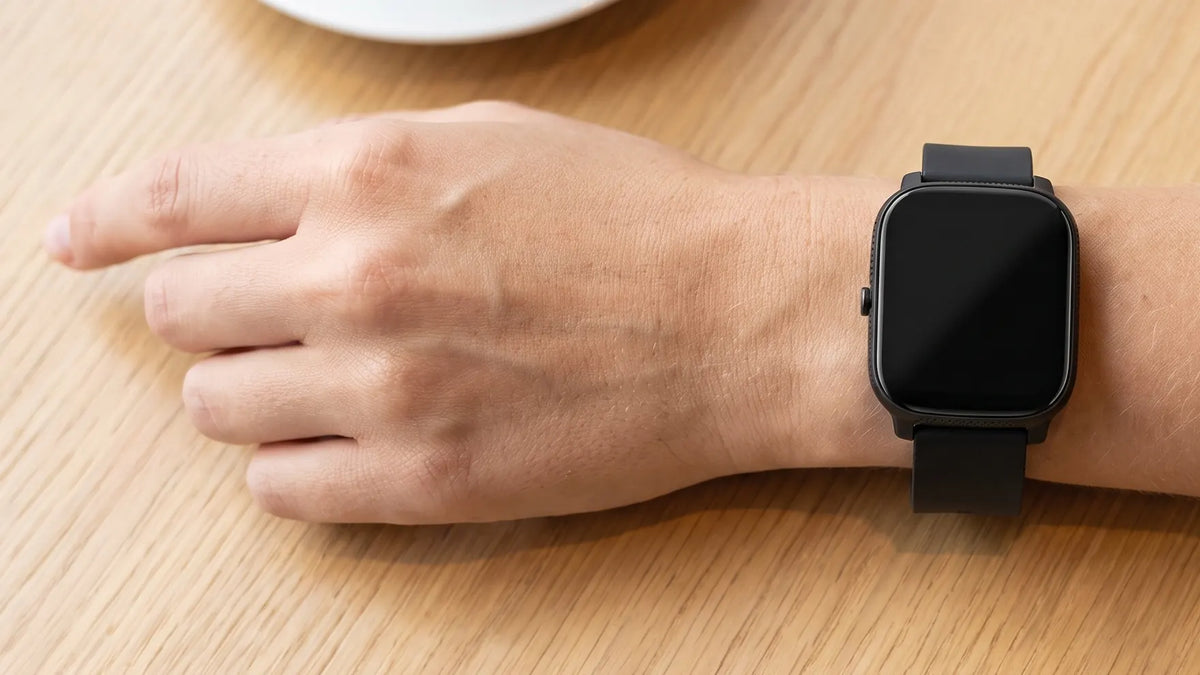 Pols met de Denver SWC184 smartwatch op een houten cafétafel, van bovenaf, met een kop koffie